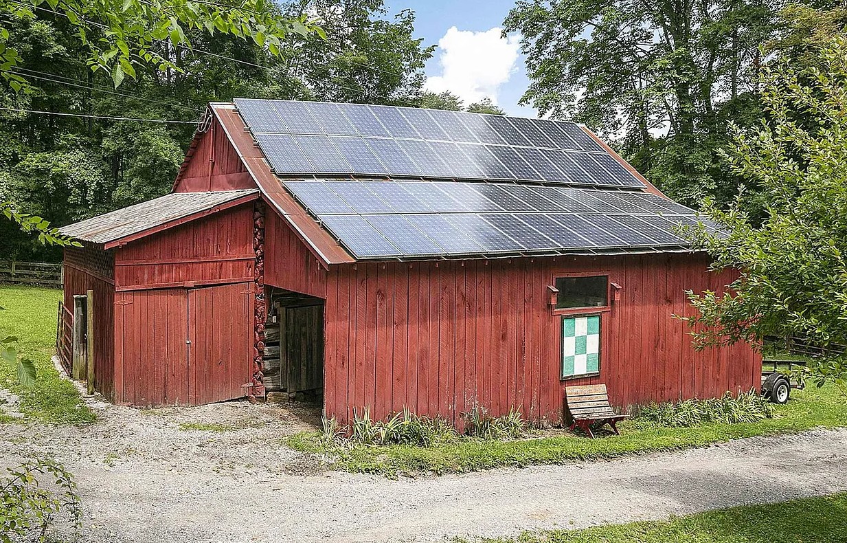Red barn with solar panels on the roof and a quilt block on its side