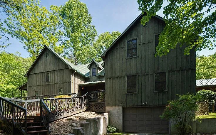 Front of the green board-and-batten farmhouse with its sunburst-railed stairway and garage